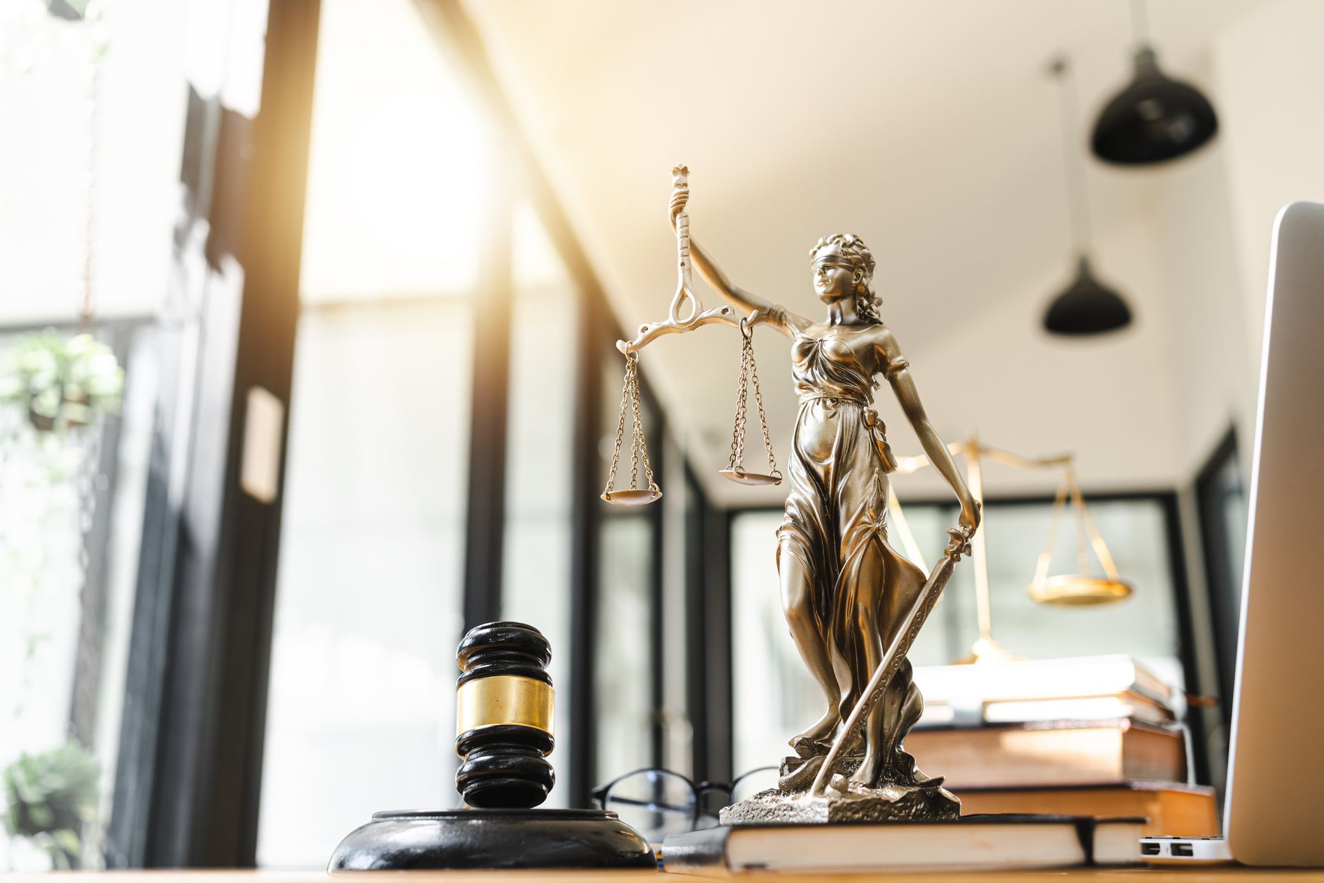 A statue of justice is sitting on a desk next to a laptop and a gavel.