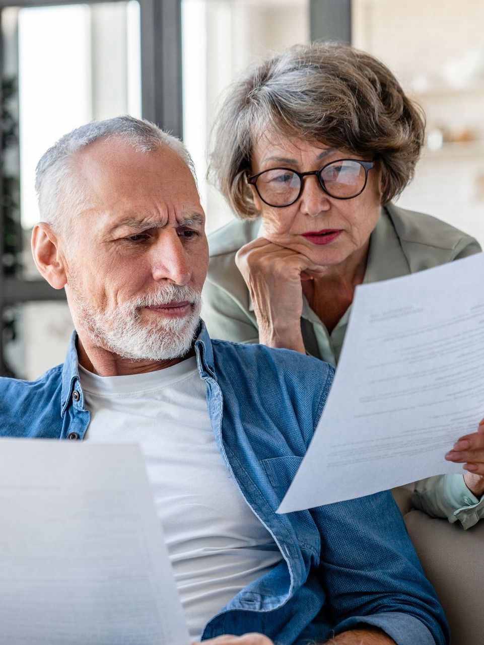 An elderly couple is sitting on a couch looking at a piece of paper.