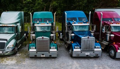 A row of semi trucks parked next to each other in a gravel lot.
