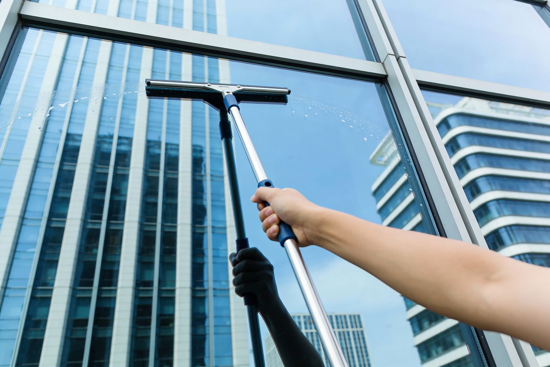 Hand cleaning tall glass building windows with a squeegee