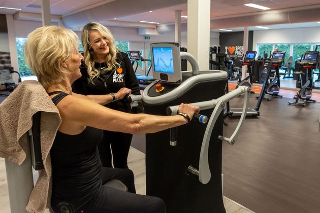 Een vrouw gebruikt een machine in een sportschool terwijl een andere vrouw toekijkt.