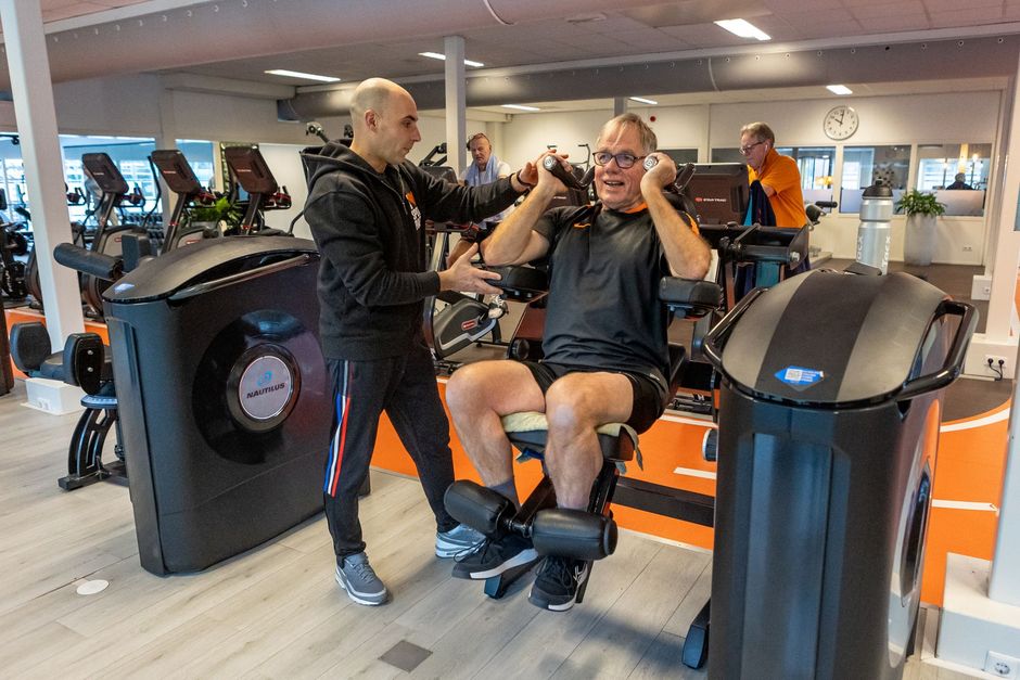 Een man praat met een andere man terwijl hij op een machine in een sportschool zit.