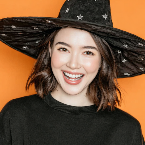 Woman in black witch hat smiles against orange backdrop.