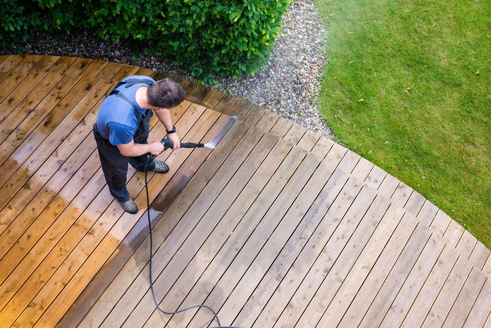 A man is cleaning a wooden deck with a high pressure washer.