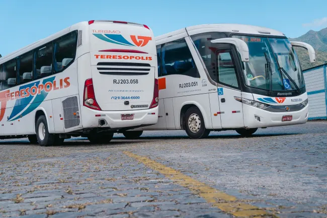 Dois ônibus brancos da Viação Teresópolis estão estacionados um ao lado do outro em um estacionamento.