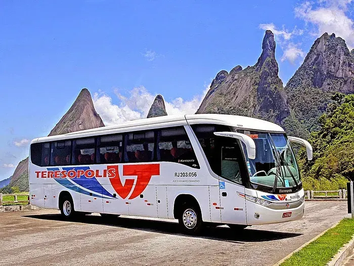 Um ônibus branco da Viação Teresópolis está estacionado na beira da estrada em frente a uma montanha.