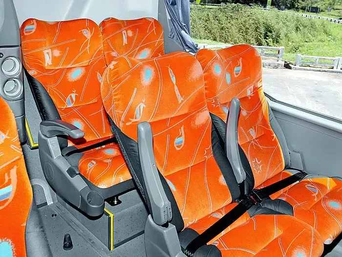 Uma fileira de assentos laranja em um ônibus.
