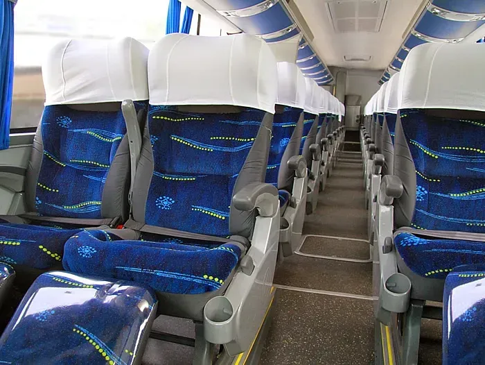 O interior de um ônibus com assentos azuis e capas brancas