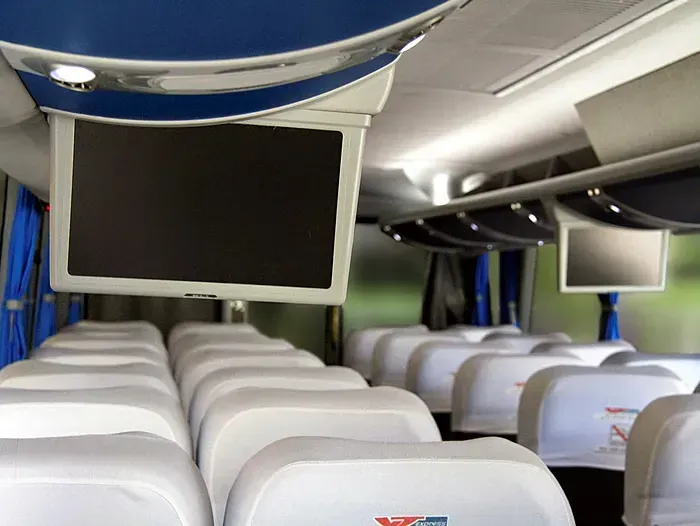 O interior de um ônibus com uma TV acima dos assentos