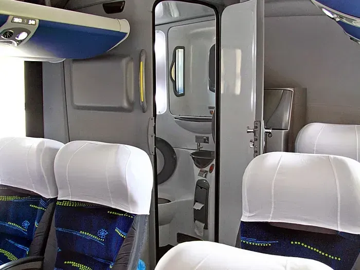O interior de um ônibus com assentos azuis e capas brancas