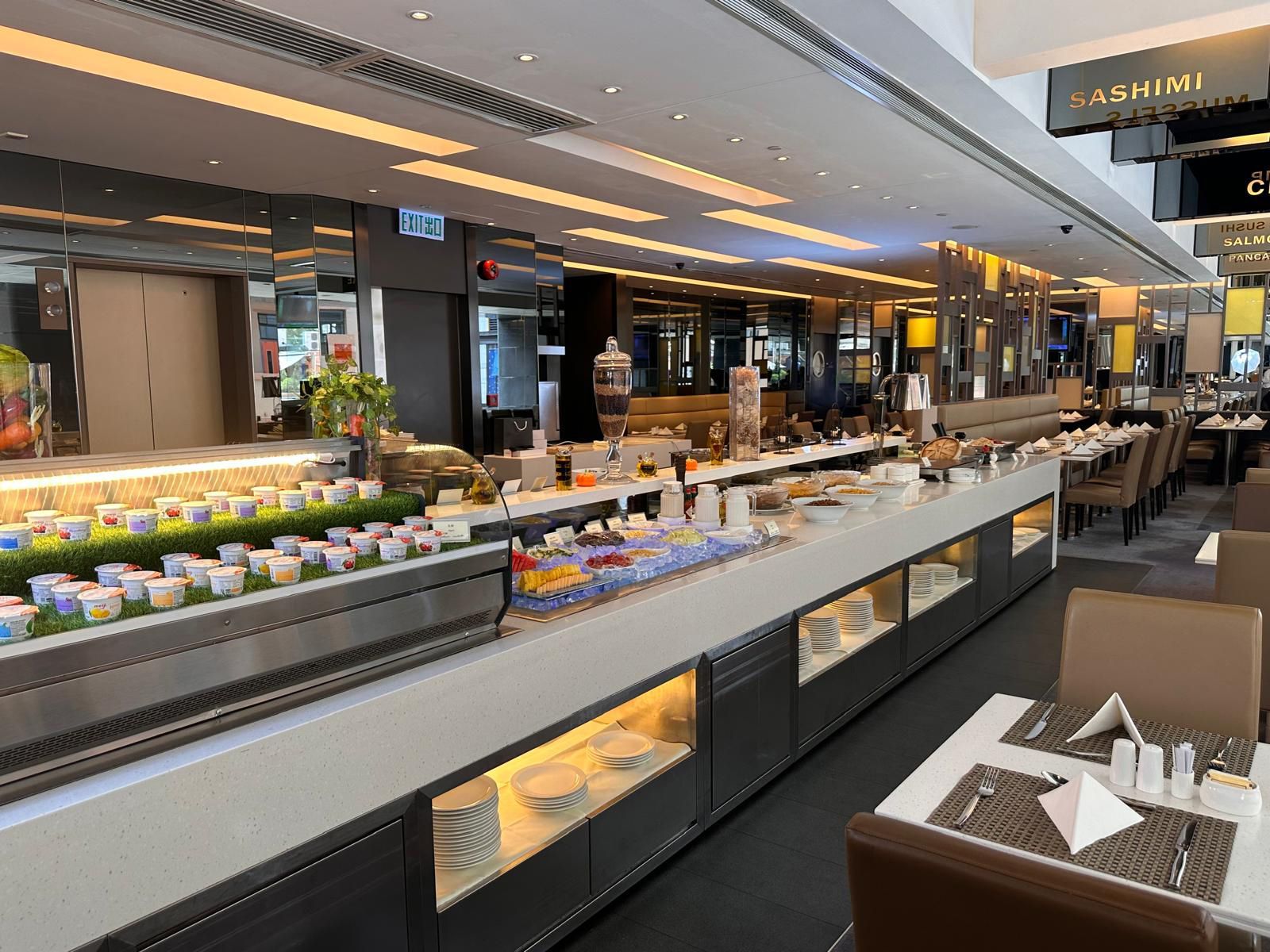 A buffet at a restaurant with various food items displayed. Long, white countertops with food, and tables with chairs.