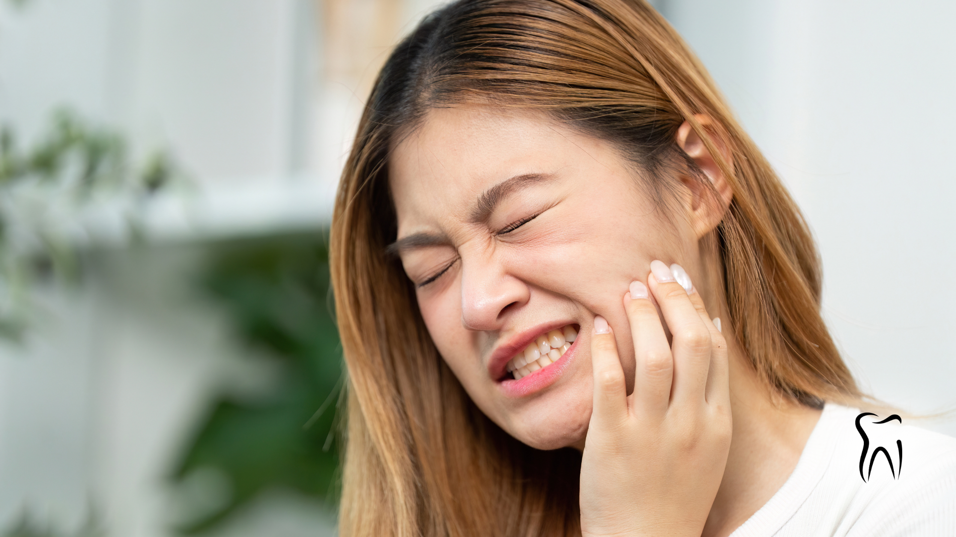 Woman with hand on cheek, grimacing in pain, likely from toothache.