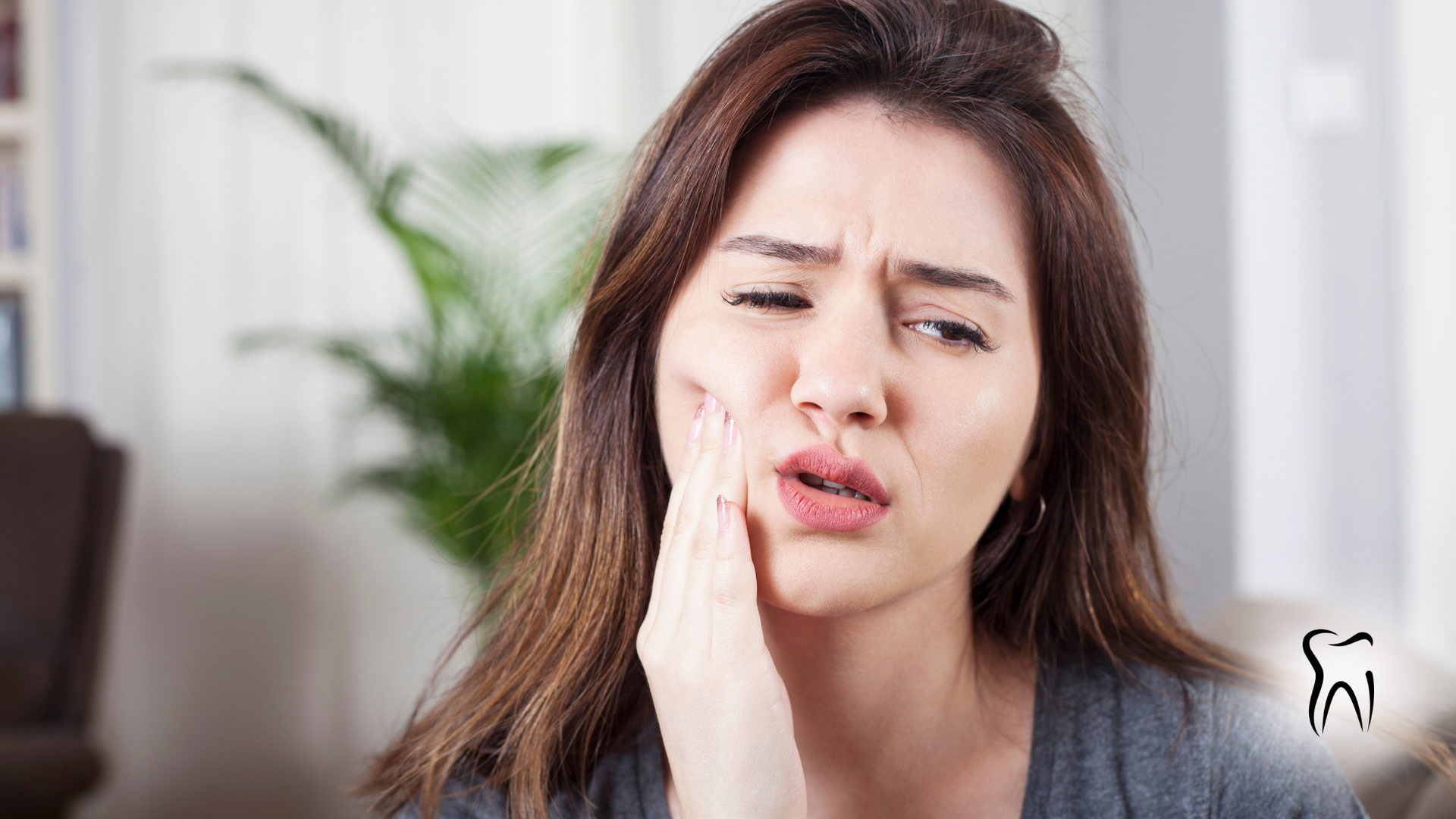 Woman with hand on cheek, grimacing, indicating possible toothache.