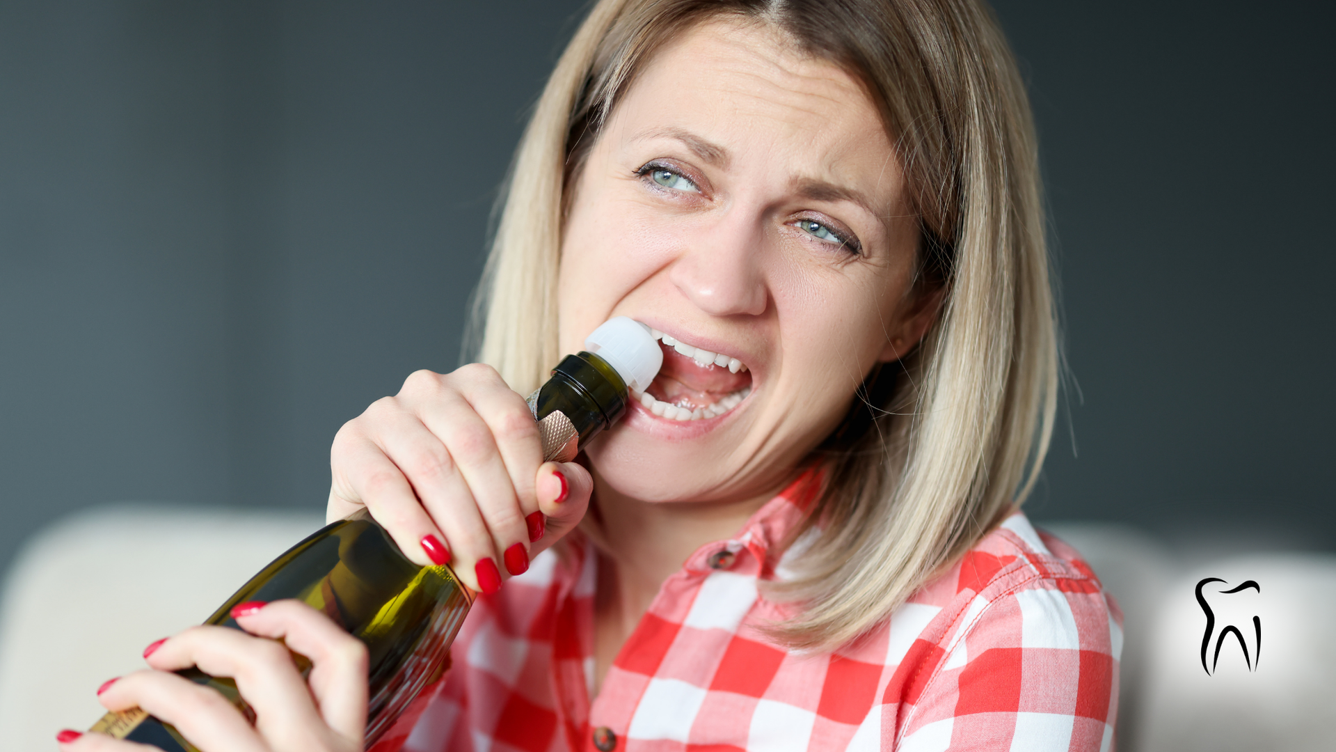 Woman attempting to open champagne bottle with her teeth, with pained expression. Red plaid shirt, blurred background.