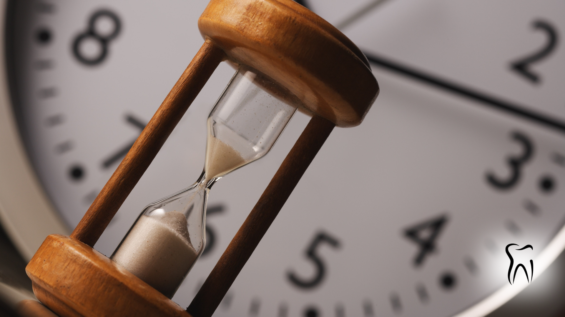 Hourglass with sand draining, in front of a clock face.