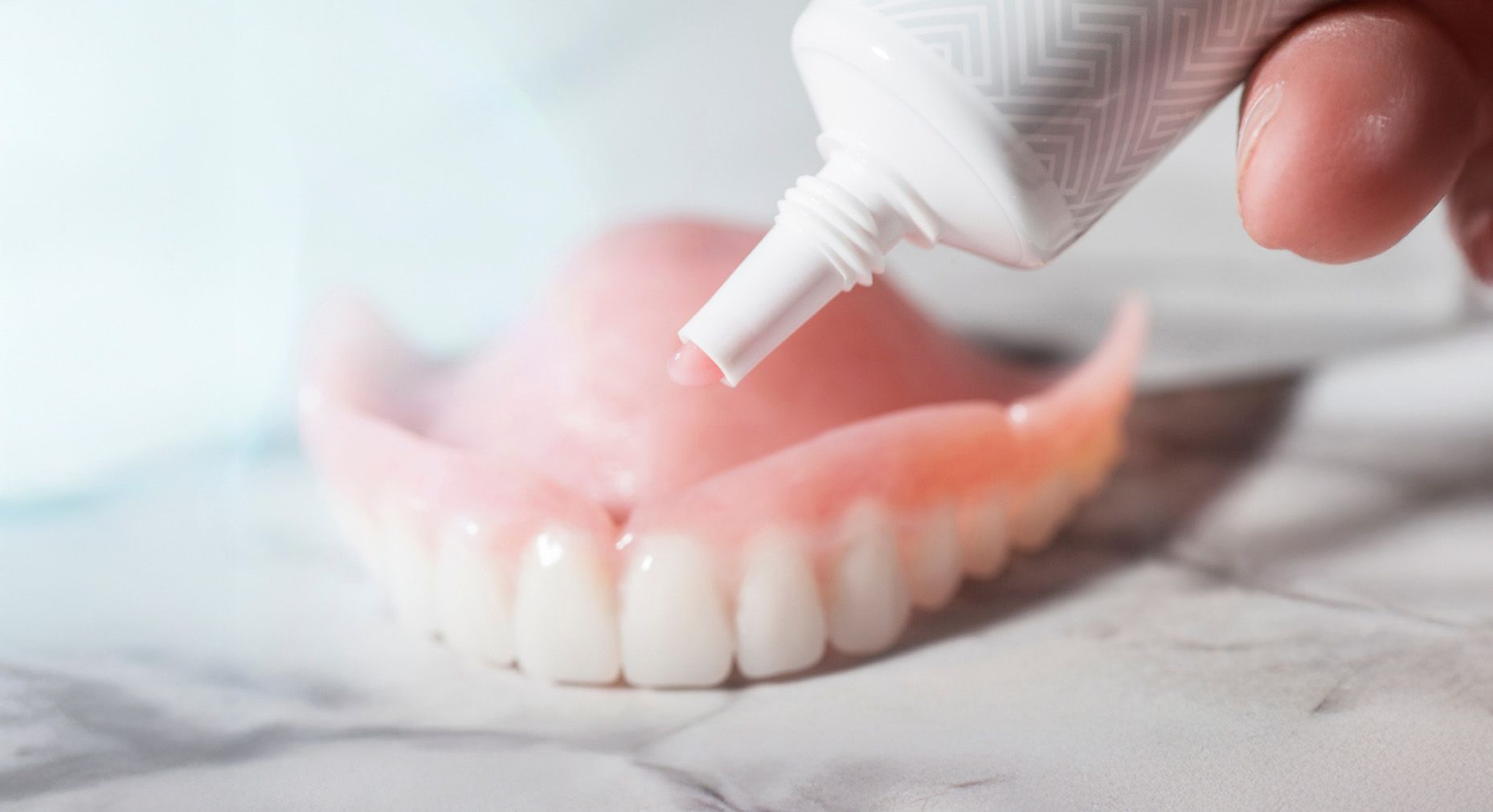 A person applies denture adhesive to a pink upper denture.
