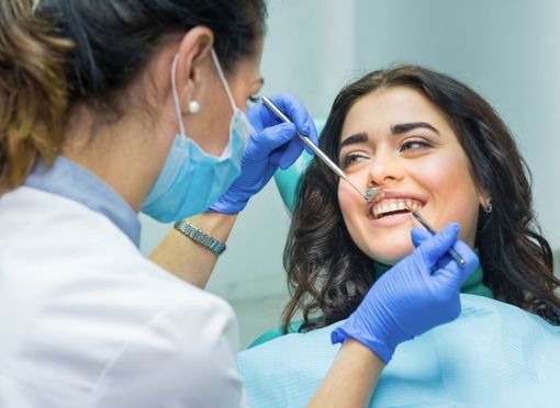 Dentist examining a smiling woman's teeth with dental tools in a bright office.
