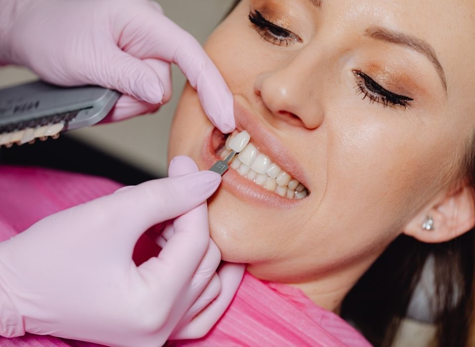 Dentist comparing tooth shade to a guide with a patient. Pink gloves, close-up, indoor setting.