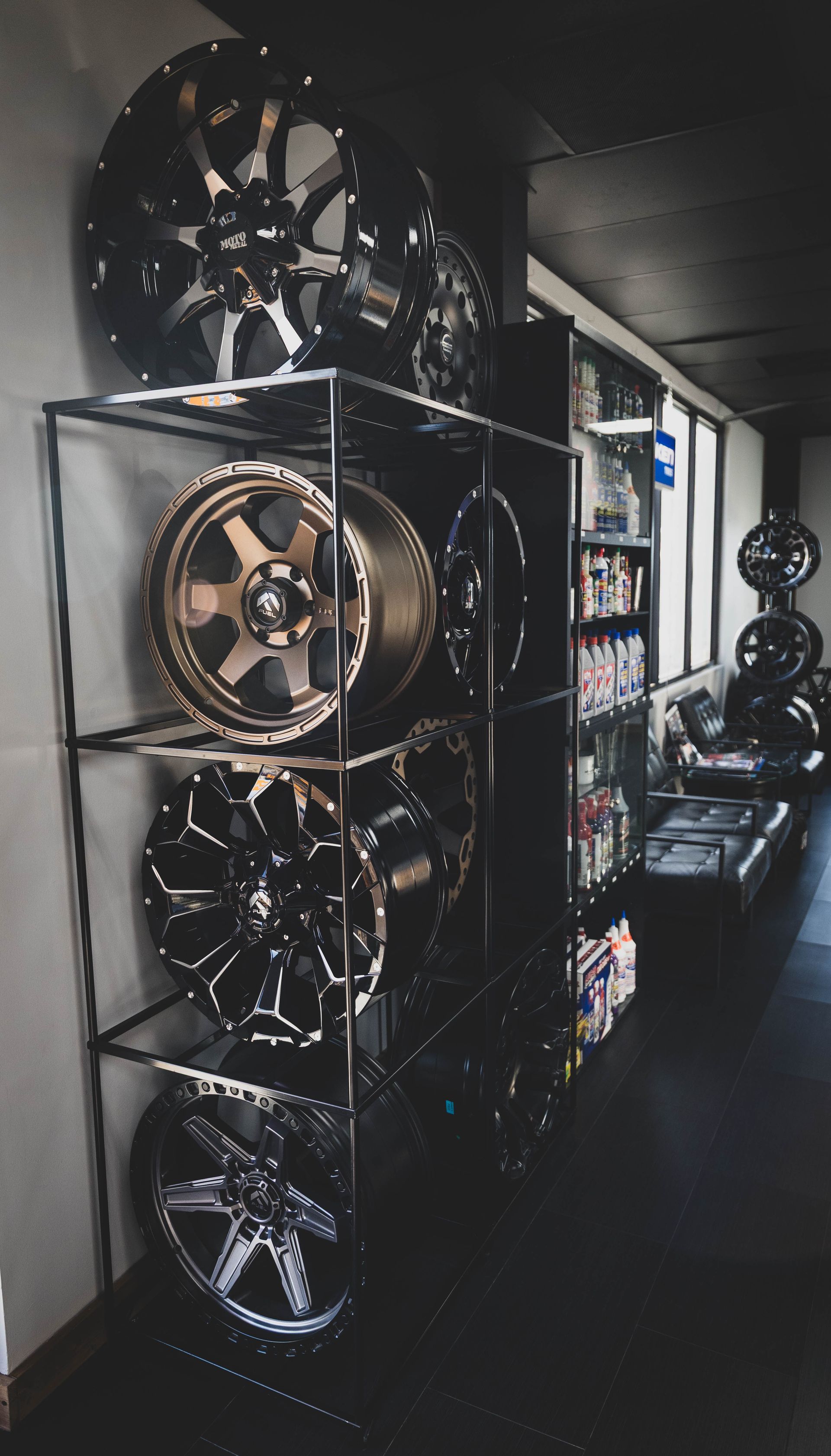 Shelves displaying various car rims in a shop, mostly black and gold, with some additional rims on the wall. | Mountain Top Service Center