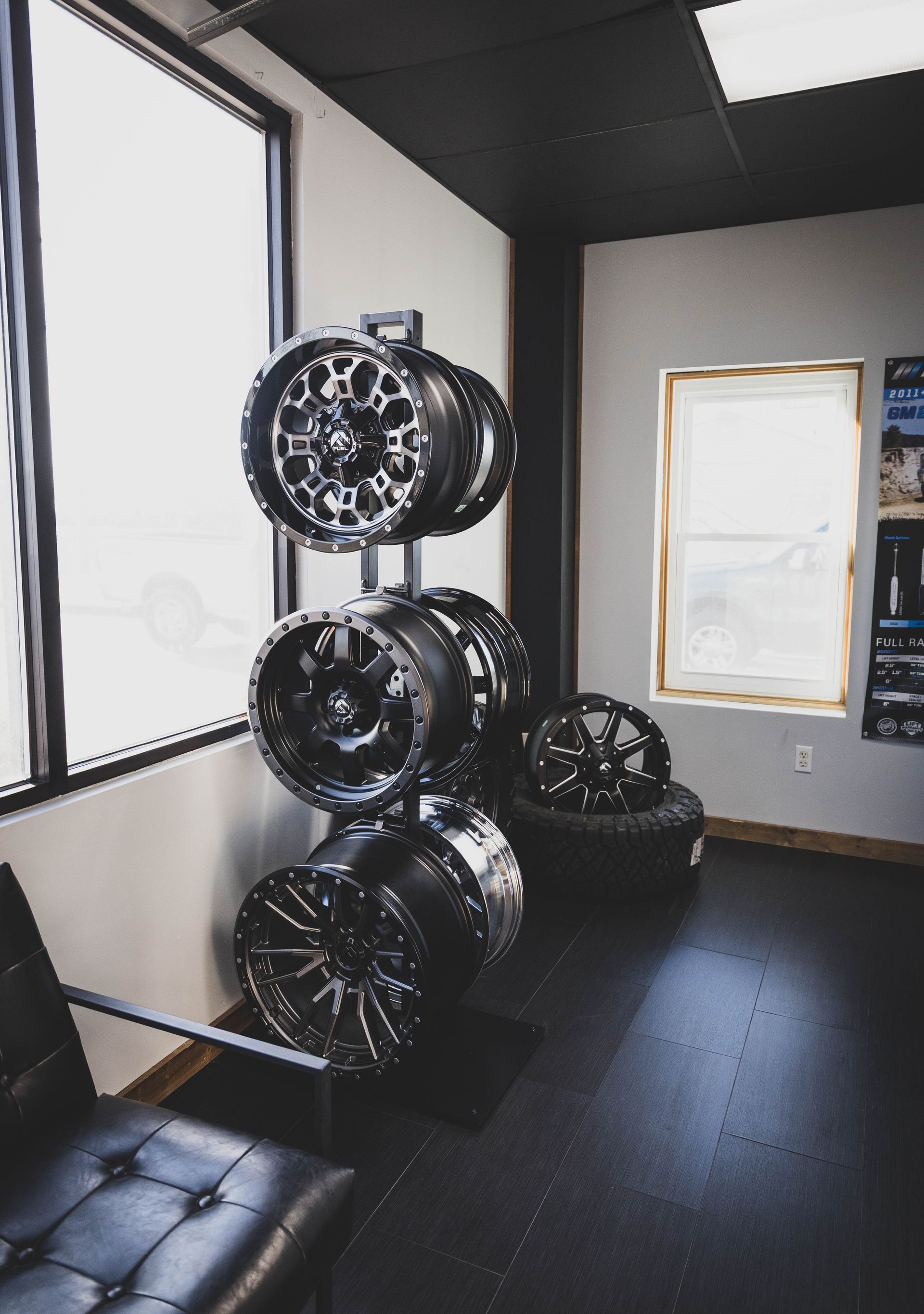 Display of black alloy wheels in a shop, with a chair and window visible. | Mountain Top Service Center