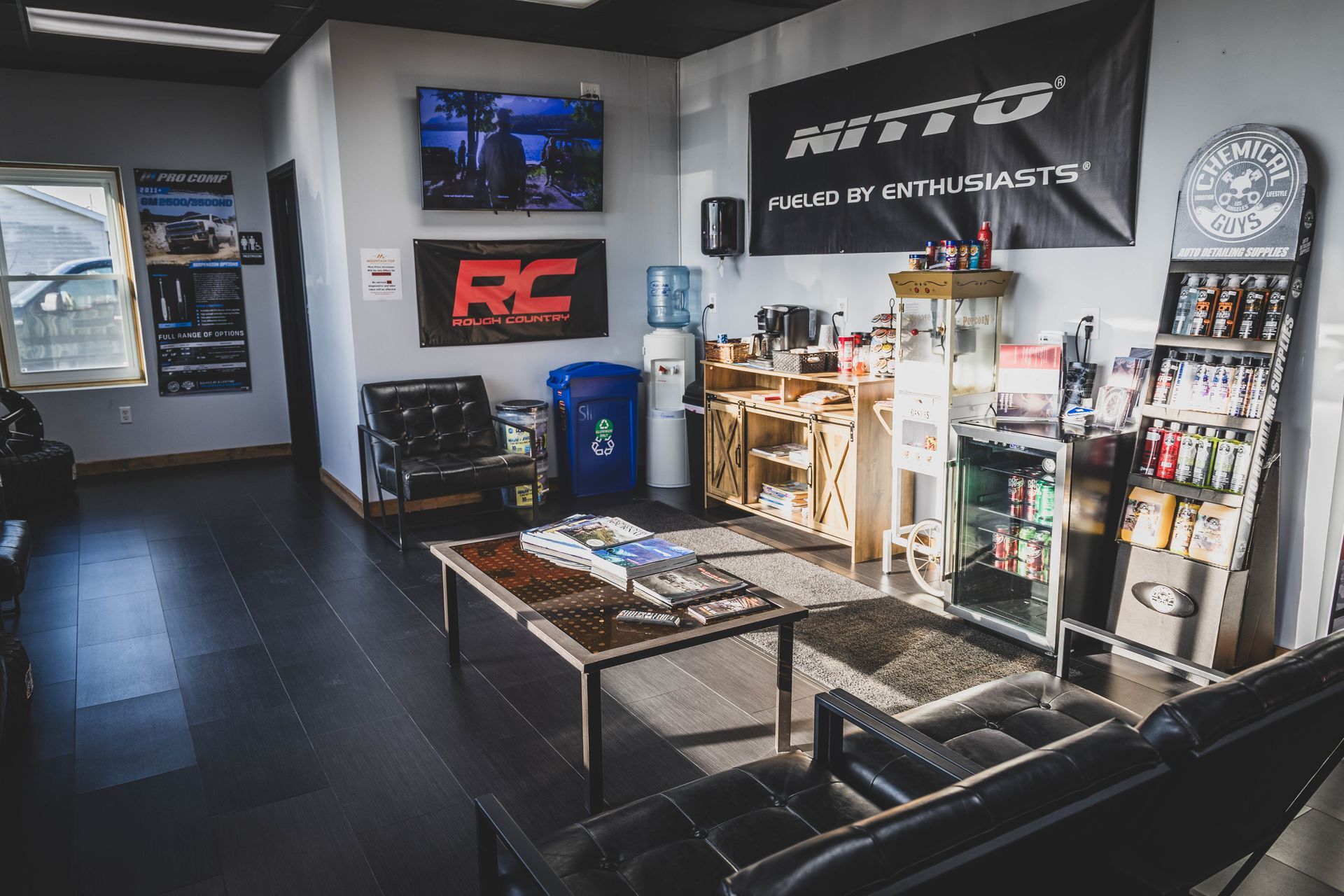Waiting area of an auto shop. Black leather couch, coffee table with magazines, and Nitro Tires banner on the wall. | Mountain Top Service Center