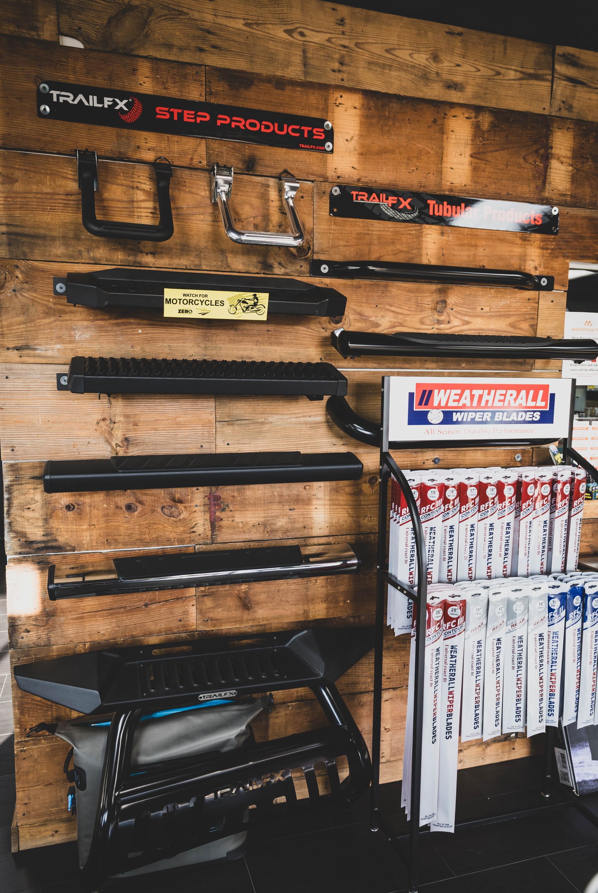 Display of truck step products on a wooden wall. Various black steps and rails are mounted. Some step products are in a display rack. | Mountain Top Service Center