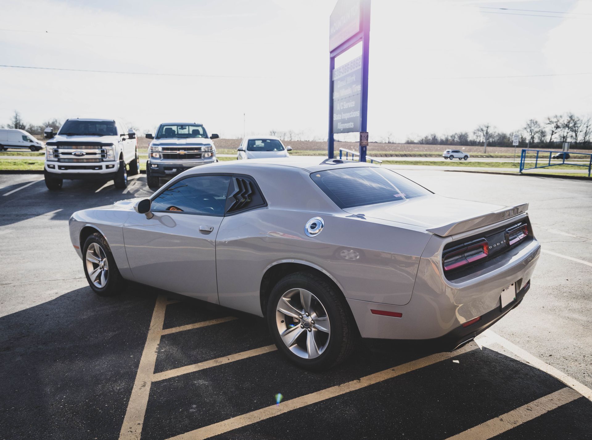 Gray Dodge Challenger parked in a lot with trucks and a sign on a sunny day. | Mountain Top Service Center