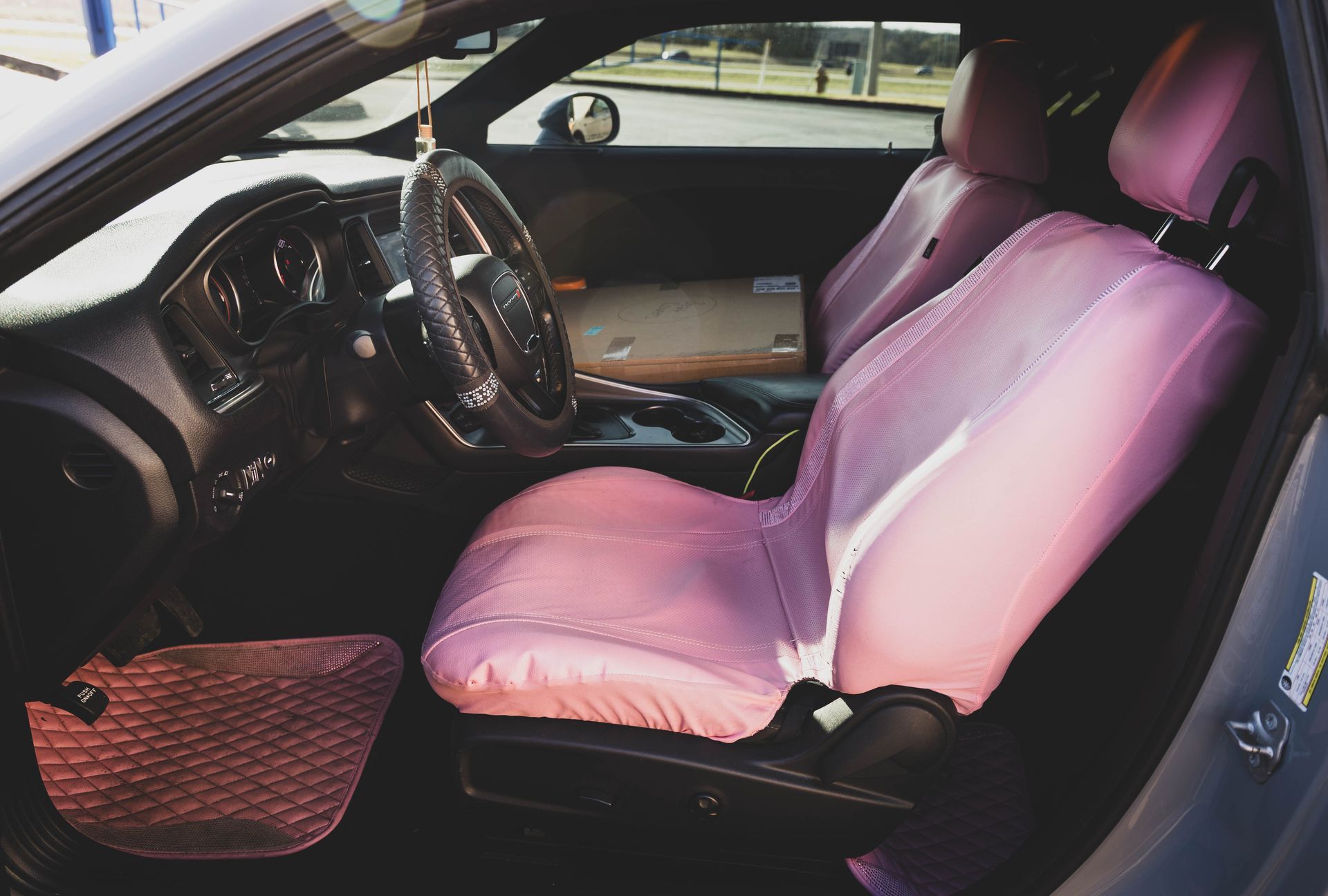 Interior view of a gray car with pink seat covers, including the steering wheel, dashboard, and floor mat. | Mountain Top Service Center