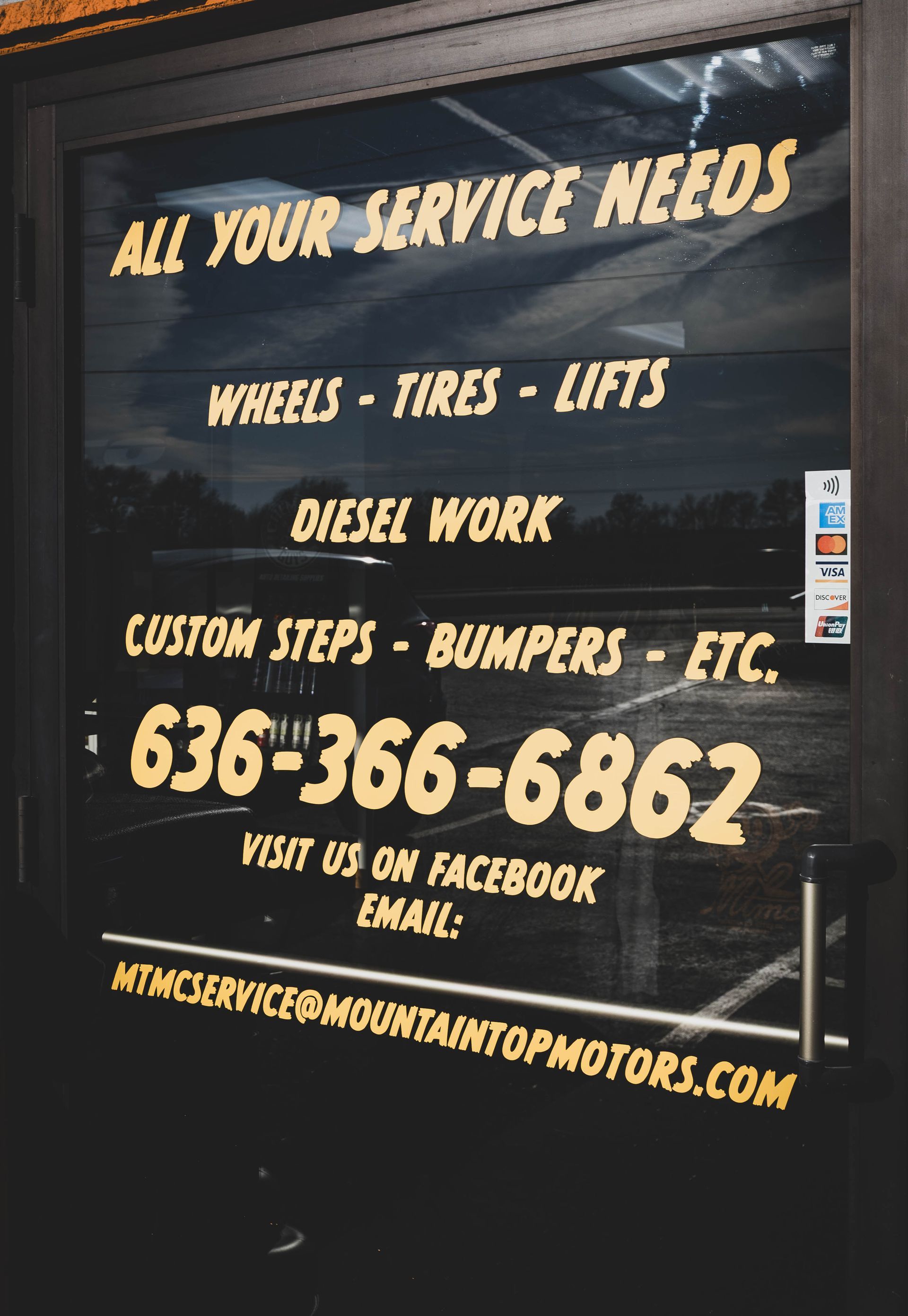 Sign on a glass door advertising auto services: wheels, tires, lifts, diesel work, custom steps, bumpers. Phone number and email are included. | Mountain Top Service Center