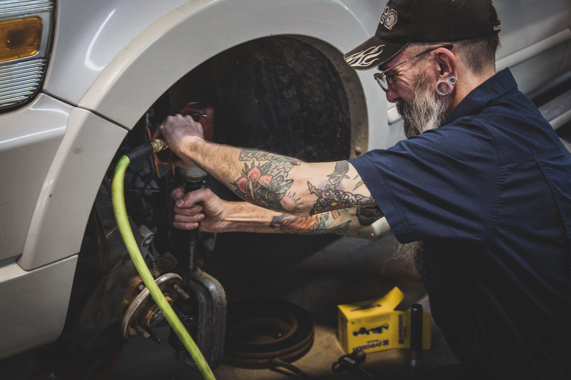 Mechanic with tattoos working on car's brakes in a garage. | Mountain Top Service Center