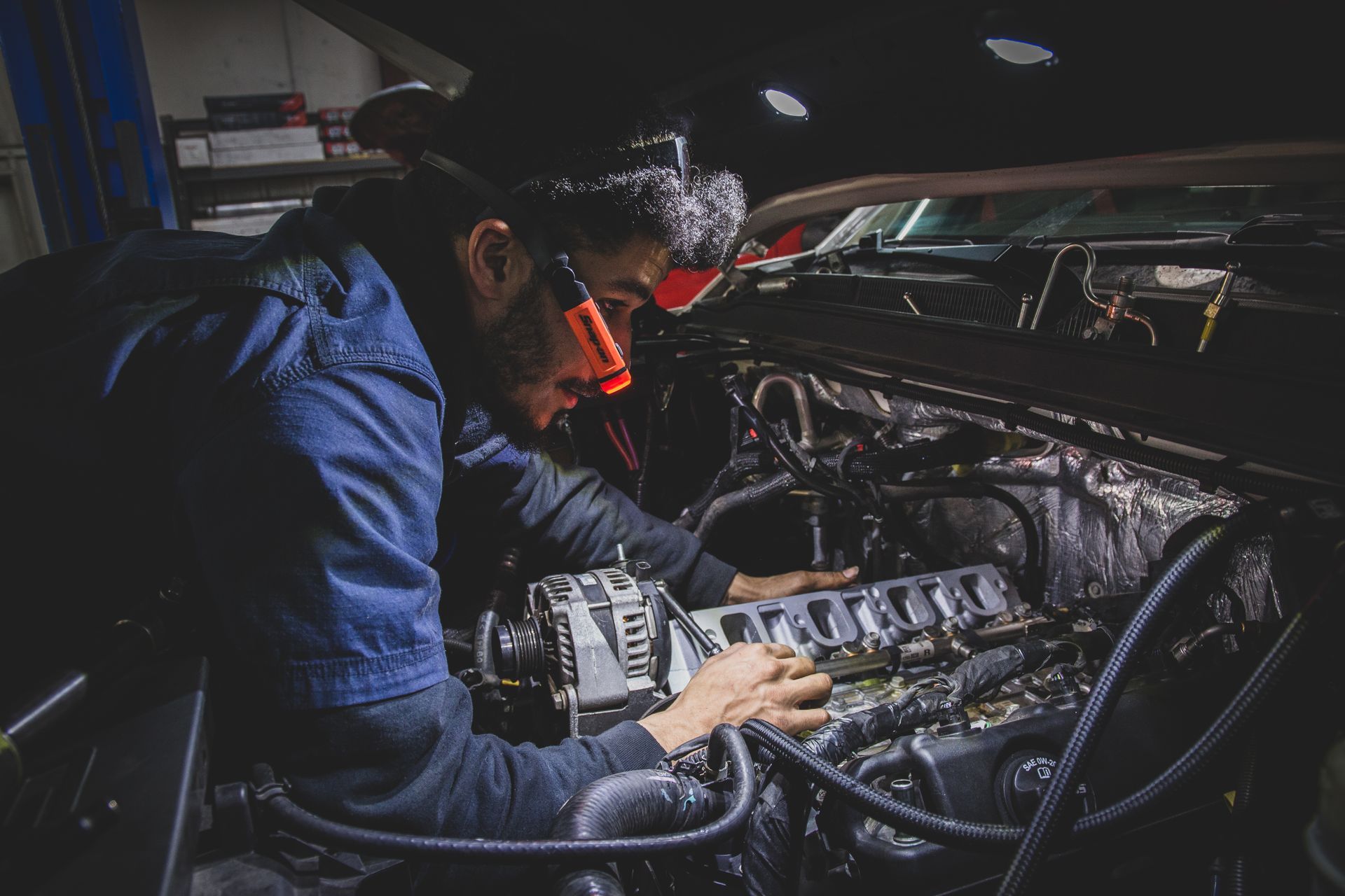Mechanic working on car engine, wearing headlamp. Dark workshop setting. | Mountain Top Service Center