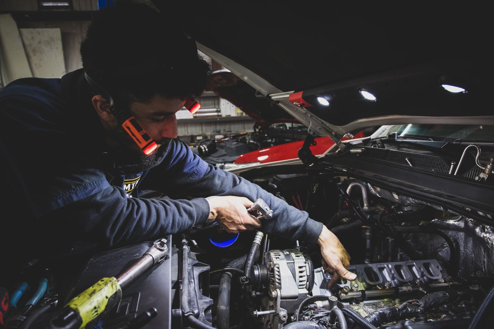 Mechanic working on a car engine under the hood in a garage, using tools. | Mountain Top Service Center