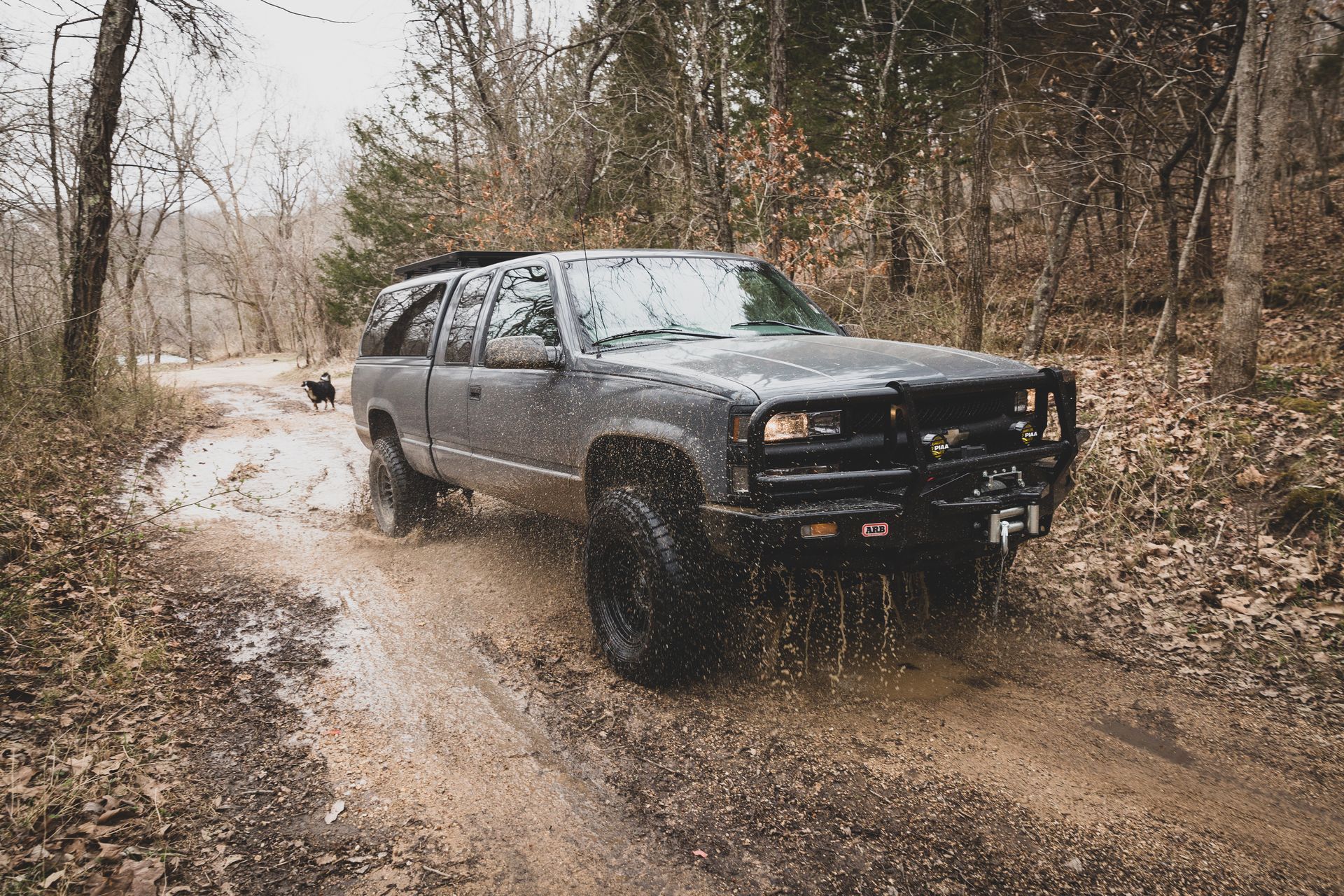 Black SUV driving through a muddy forest road, splashing water. | Mountain Top Service Center