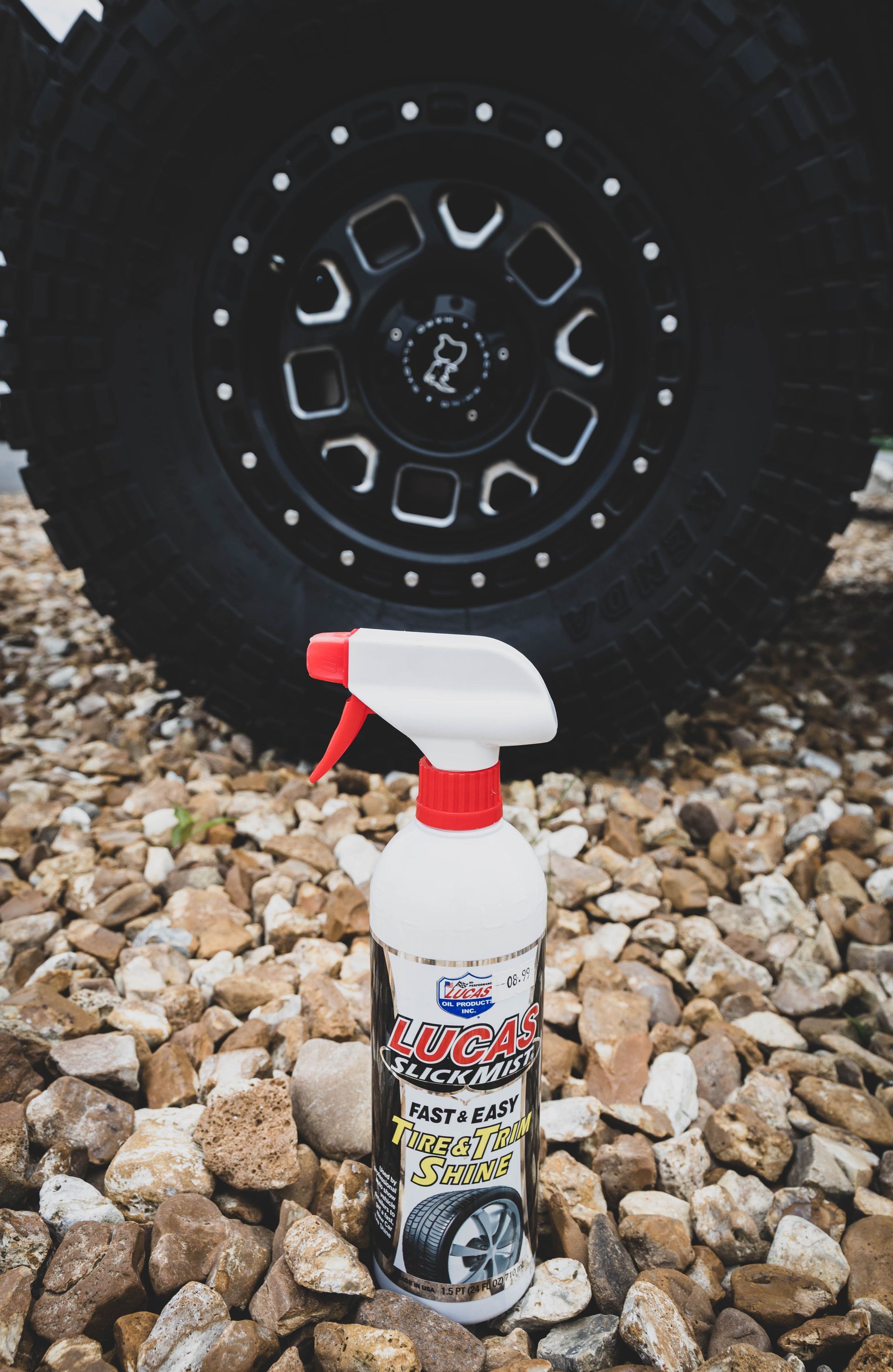 Spray bottle of tire cleaner in front of a black tire and rim on a bed of rocks. | Mountain Top Service Center