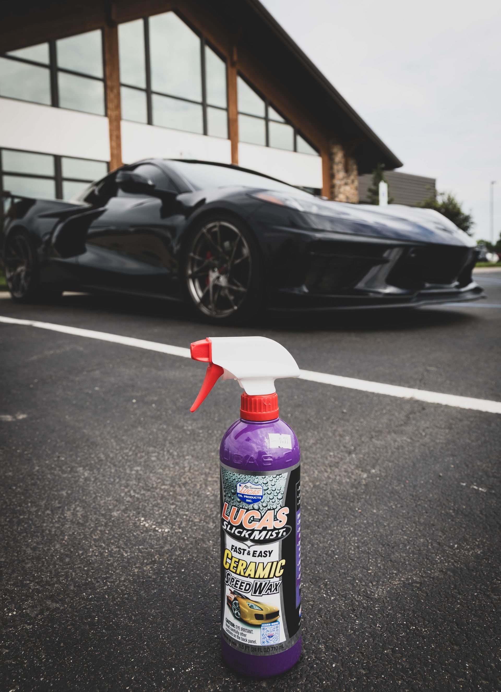 Spray bottle in focus with a black sports car in the background on asphalt parking lot. | Mountain Top Service Center