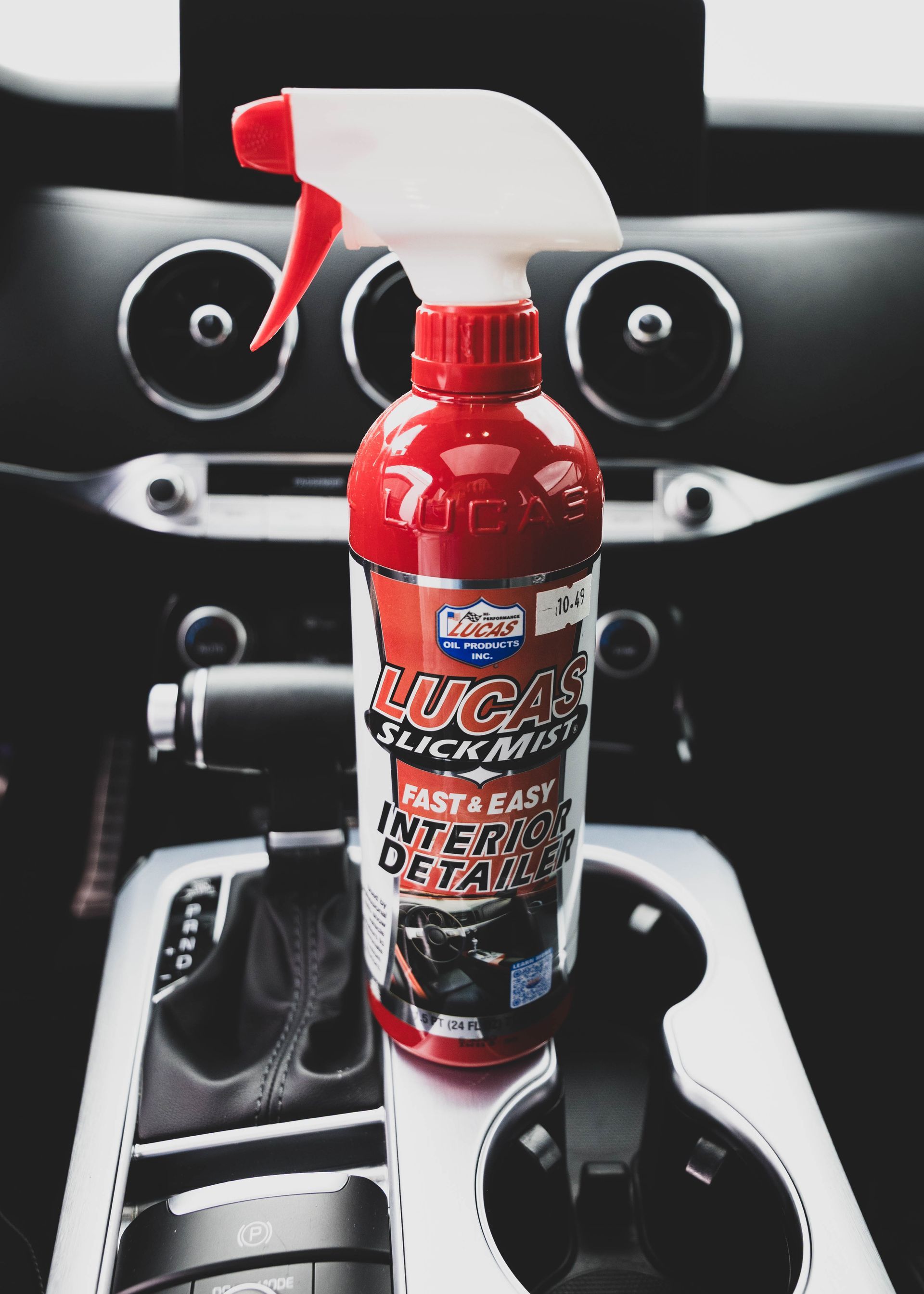 Lucas Slick Mist interior detailer bottle in a car's console. Red and white bottle with a spray nozzle. | Mountain Top Service Center