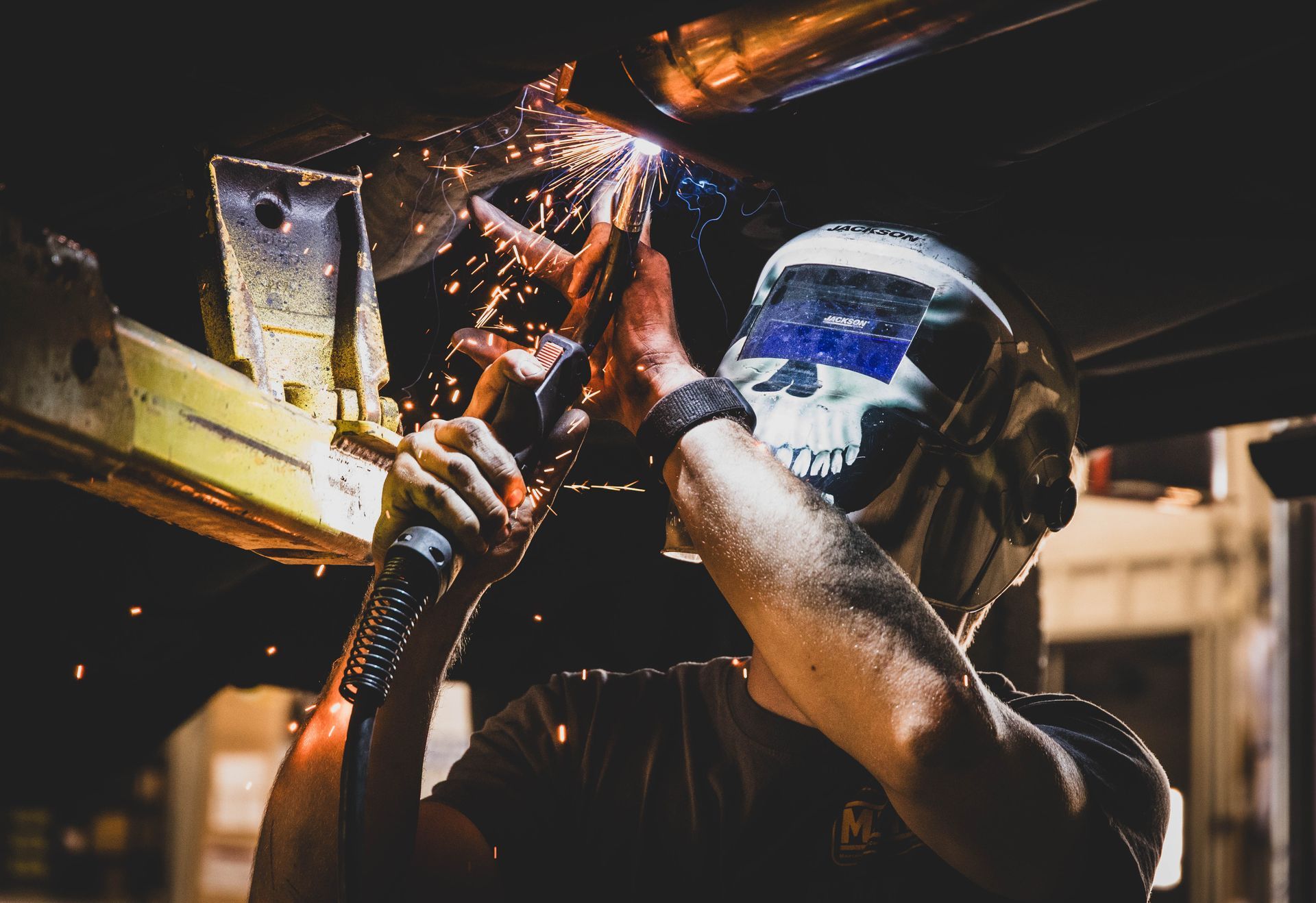 A person welding metal, wearing a skull-designed helmet, sparks flying in a garage setting. | Mountain Top Service Center
