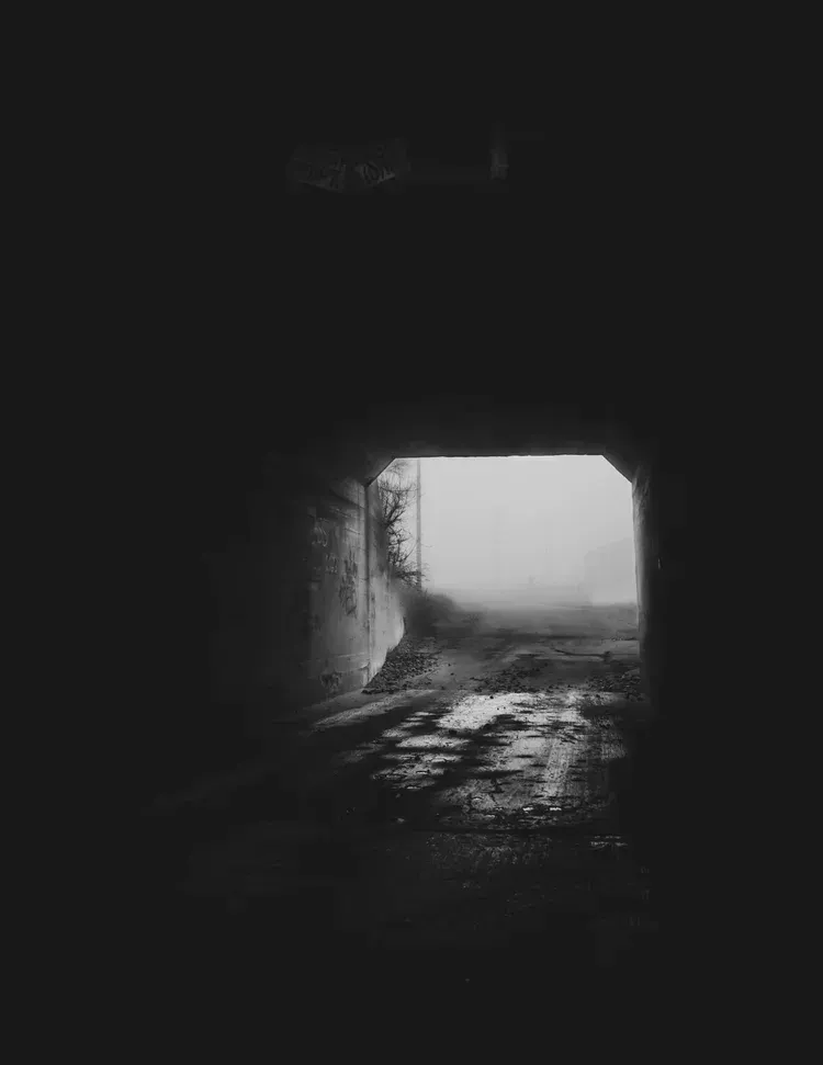 Dark tunnel leading to a misty, bright opening. Ground is wet and reflective.