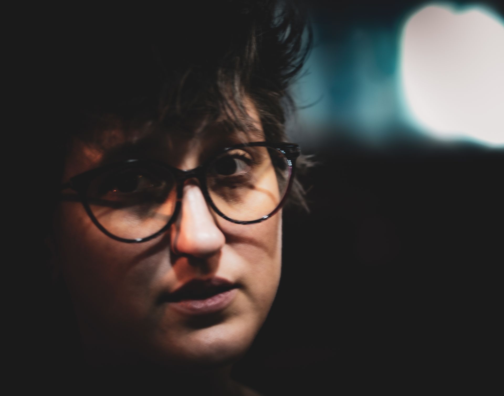 Woman with glasses looking off-camera; dark setting, focused expression.