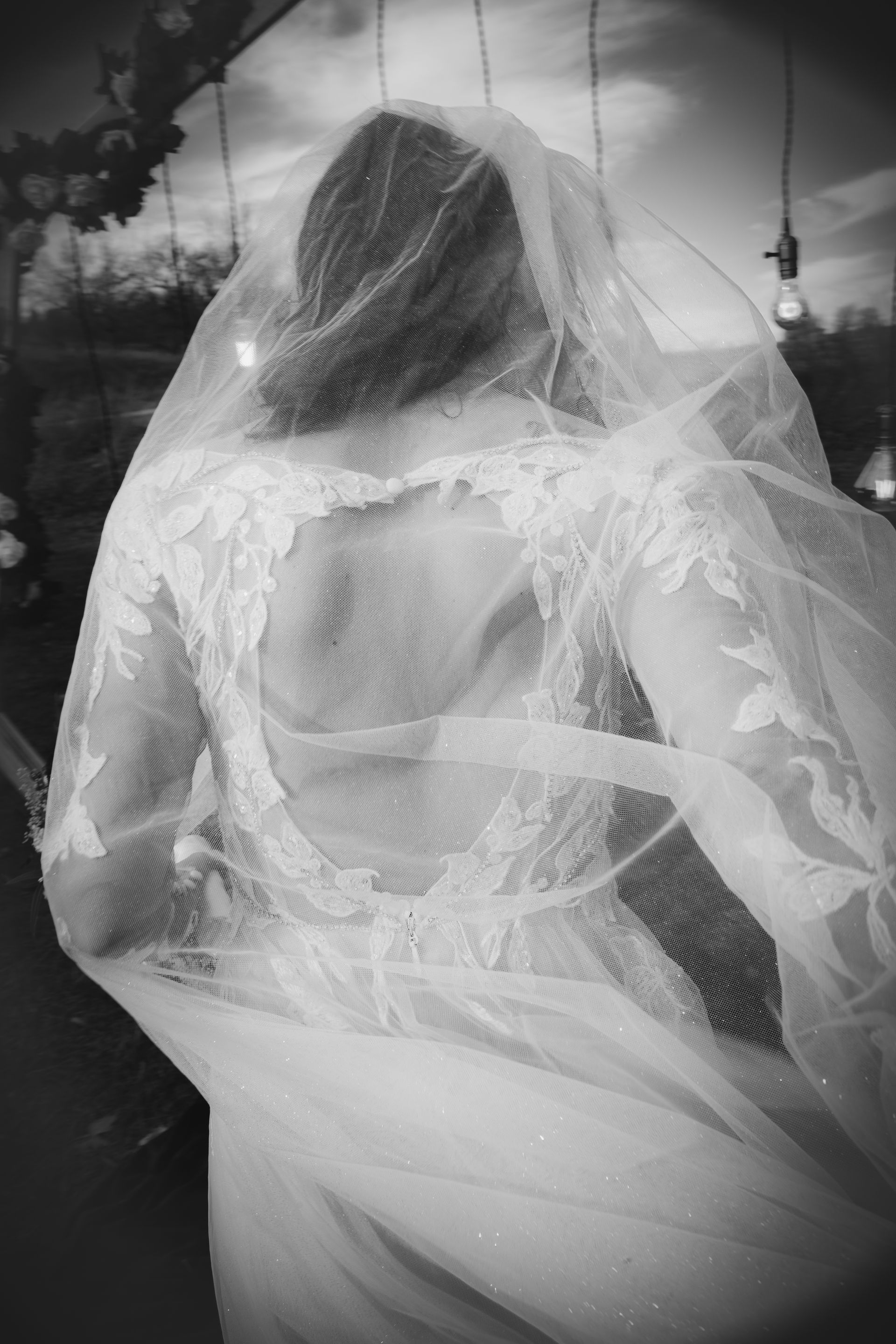Bride in a white wedding dress and veil, seen from the back, outdoors.