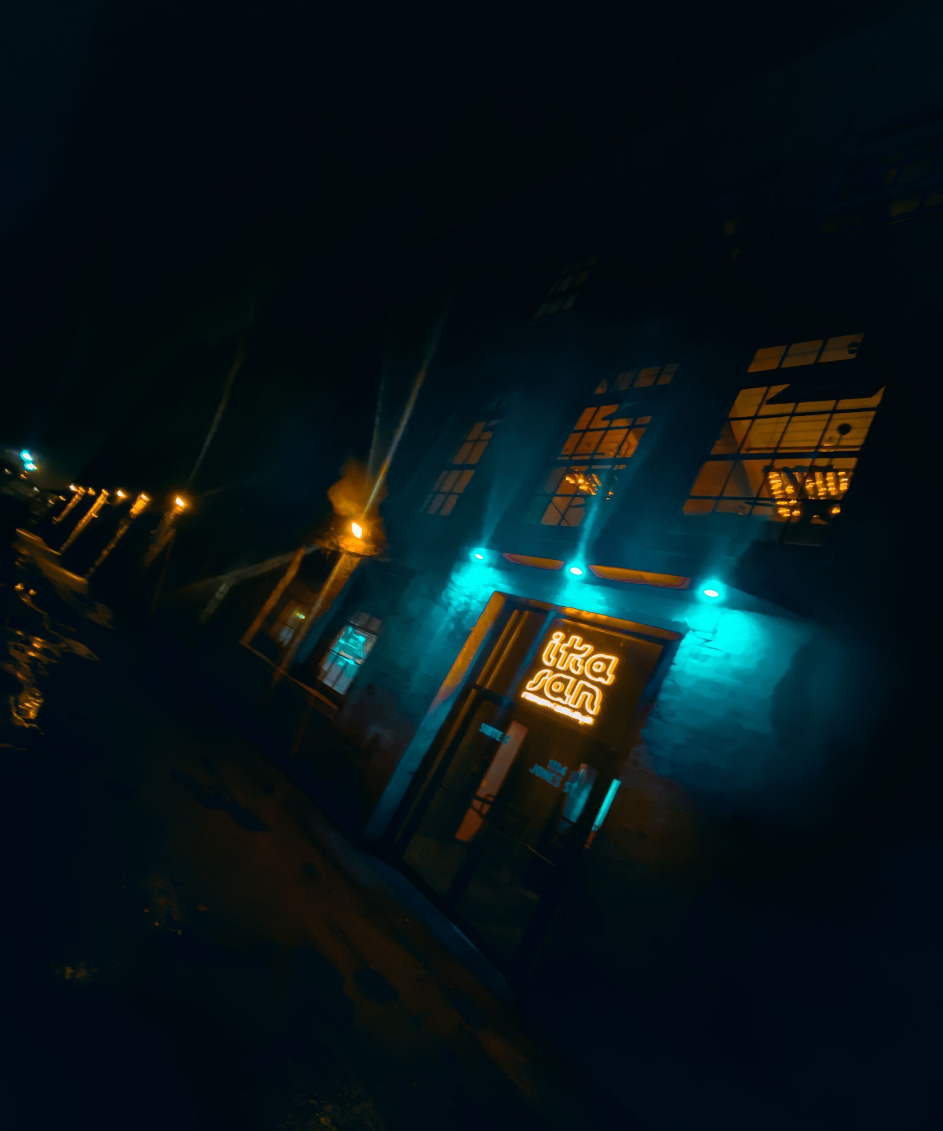 Night view of a teal-lit building with illuminated windows and a glowing entrance.