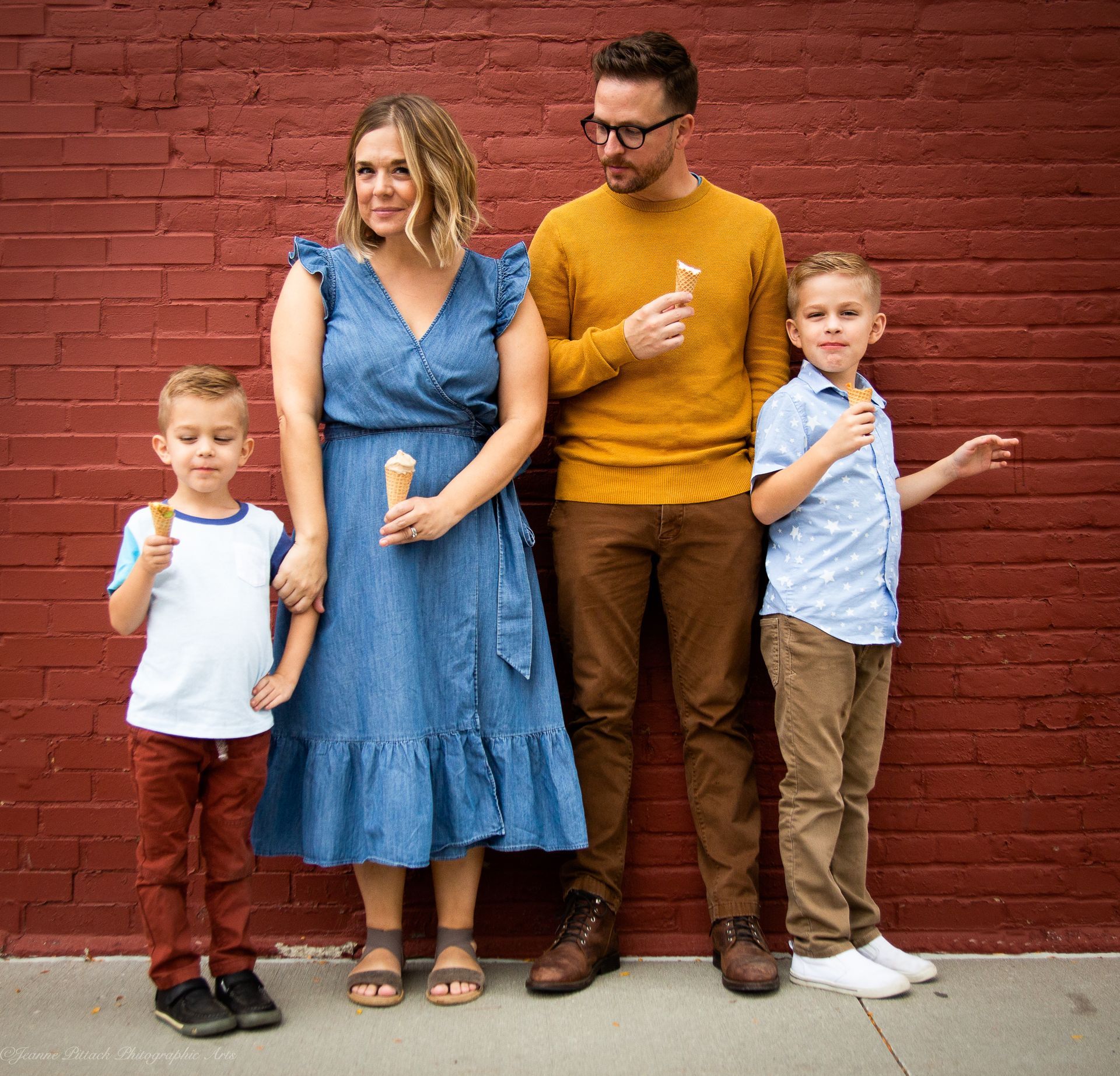 Family of four by a brick wall, holding ice cream cones.
