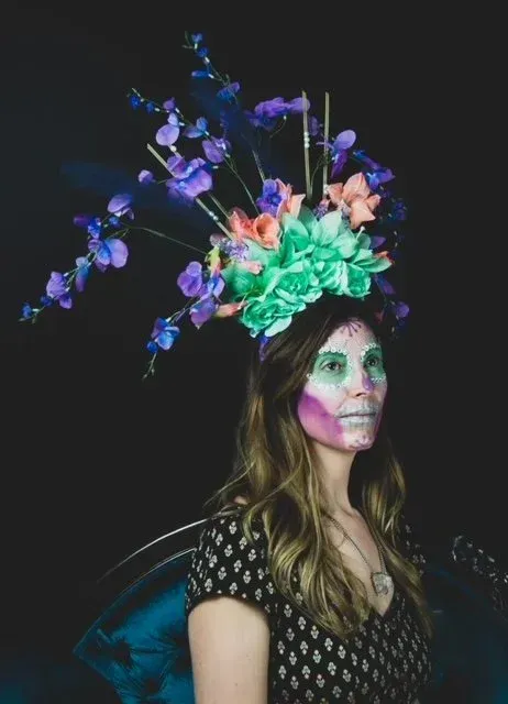 Woman in skull makeup and floral headpiece, against a dark background.