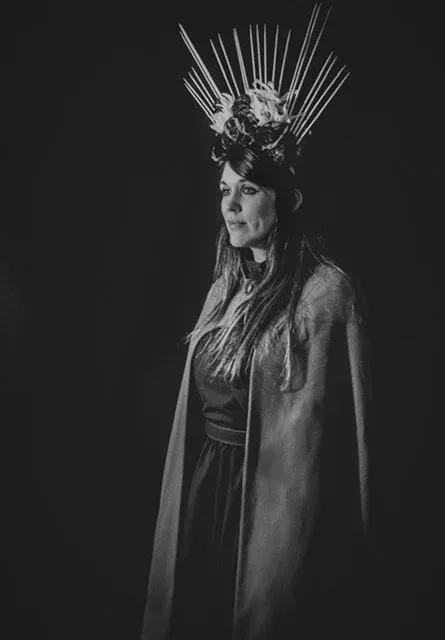 Woman in crown and cape; dark setting.