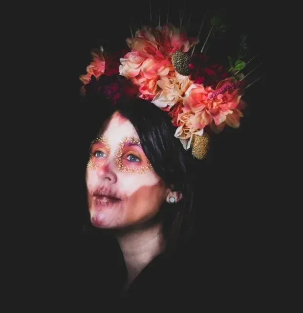 Woman with floral crown, painted face, looking upwards against a dark background.