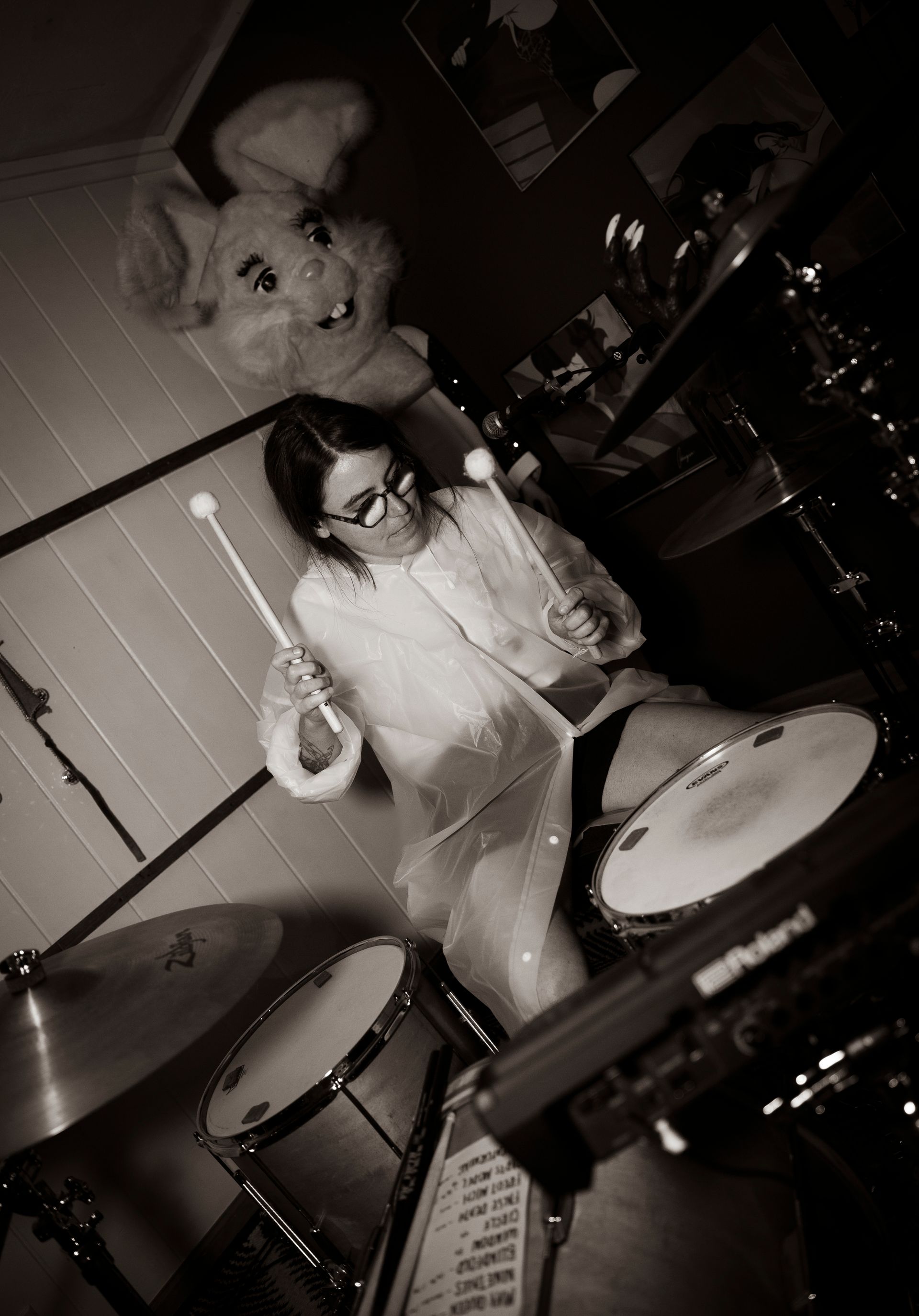 Person wearing a costume, playing the drums, with a large rabbit head behind them. Black and white photo.