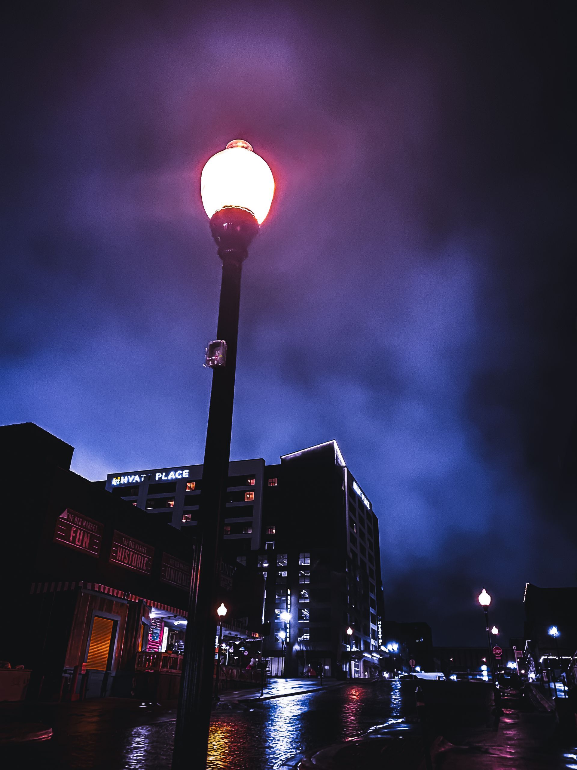 A glowing street lamp illuminates a dark city street on a stormy night.