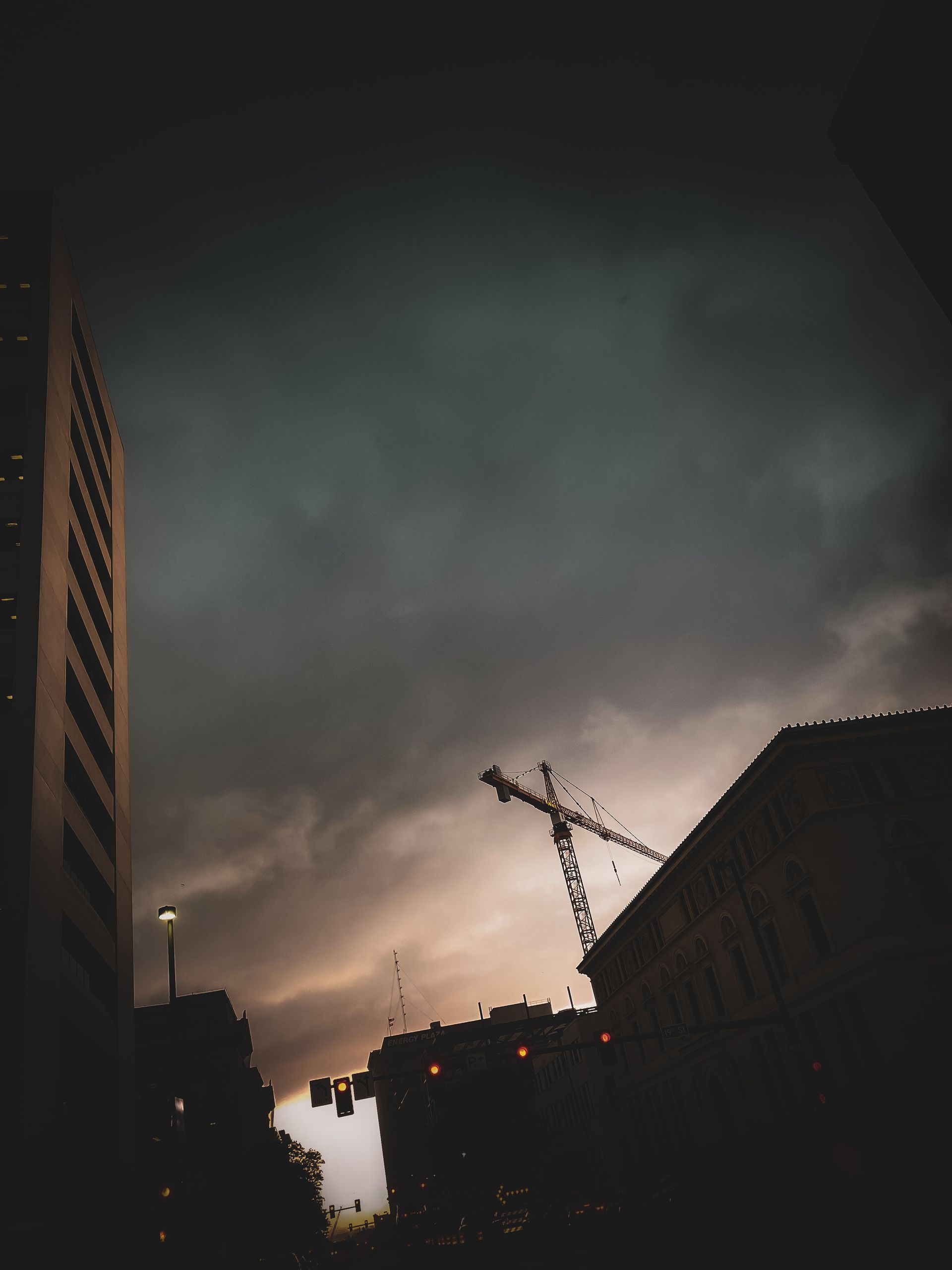 Dark cityscape with a construction crane silhouetted against a dramatic, stormy sky.