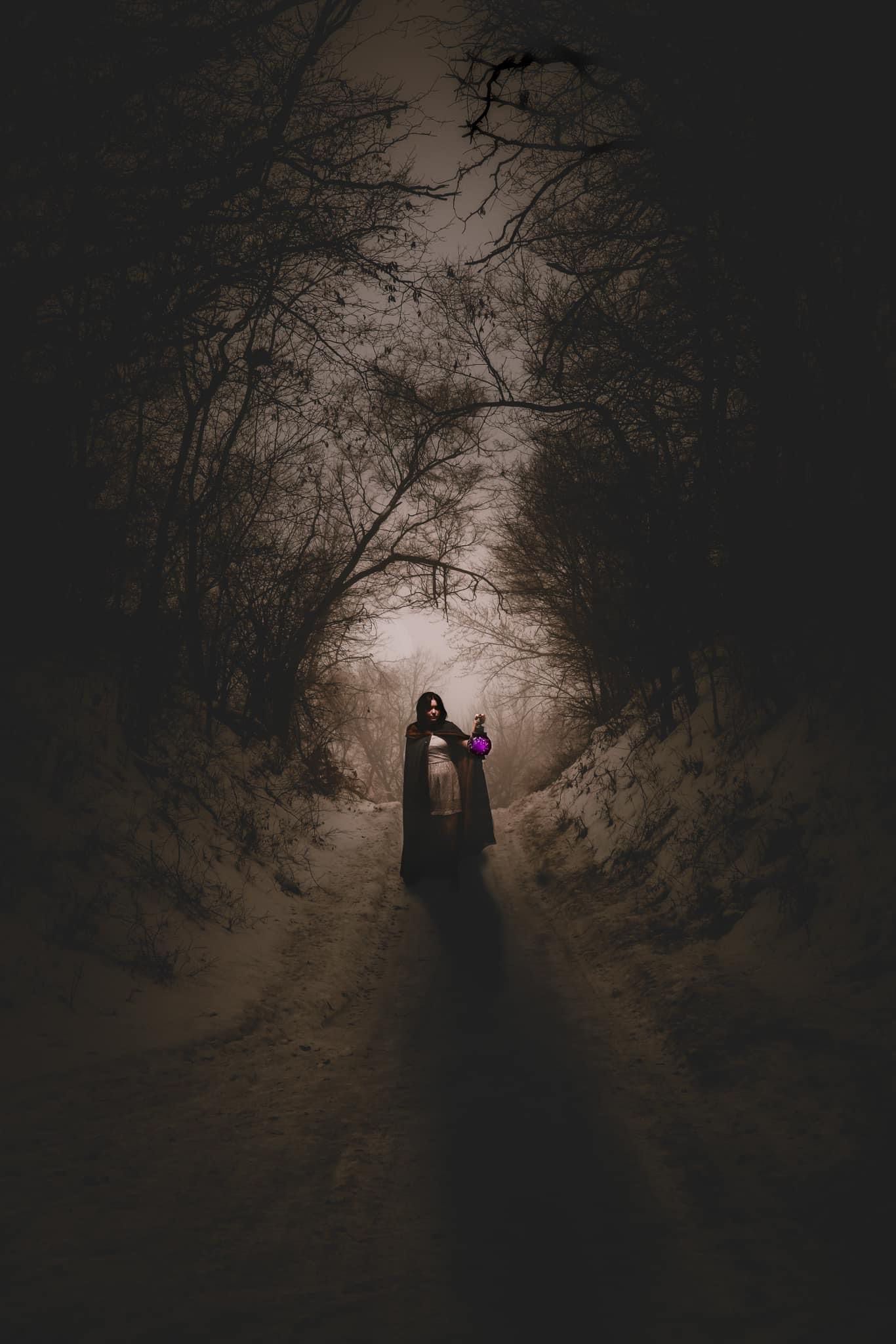 Woman walking down a dark path in a forest, holding a bouquet.