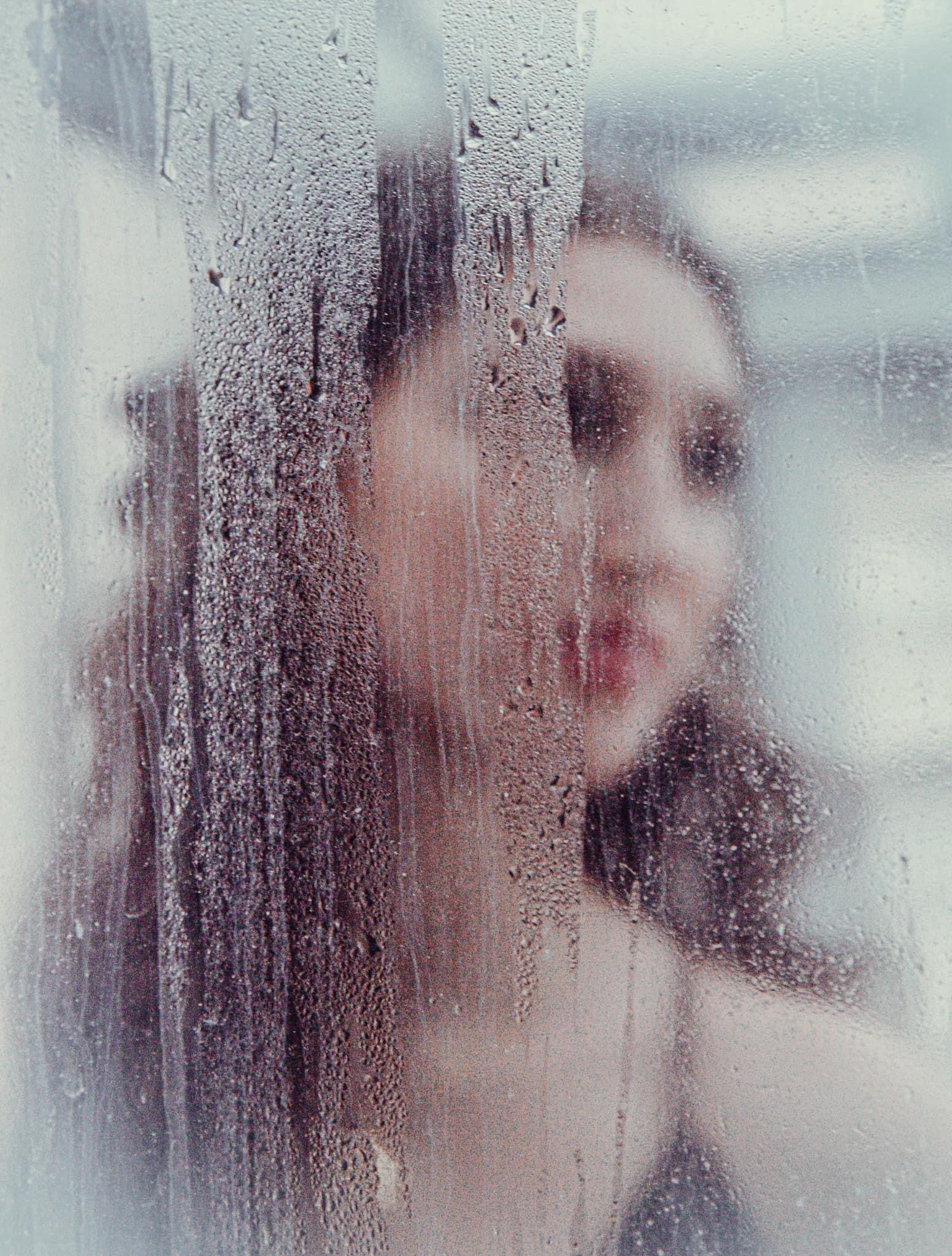 Woman with red lips, seen through a foggy glass window covered in water droplets.